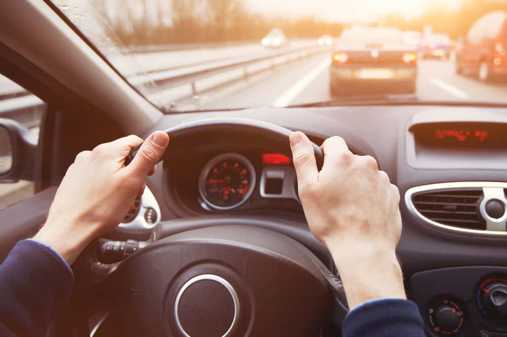 person driving car safely with two hands on steering wheel