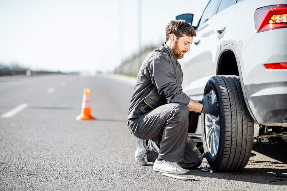 young man helping change tire as part of roadside assistance help