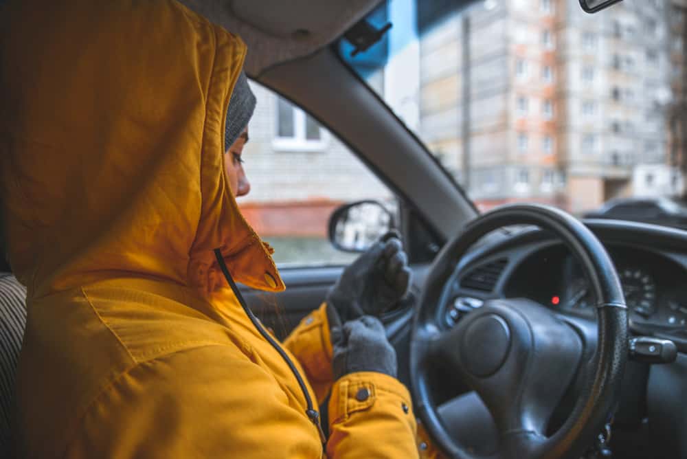 woman bundled up in yellow coat behind steering wheel of car