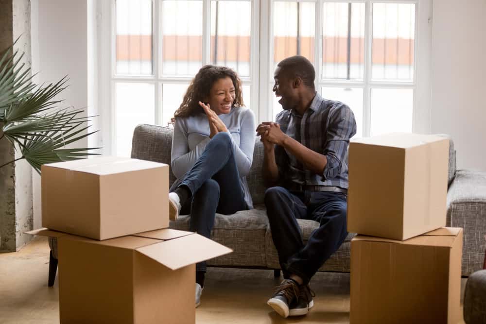 Happy African American couple sits on couch in front of window with moving boxes around them