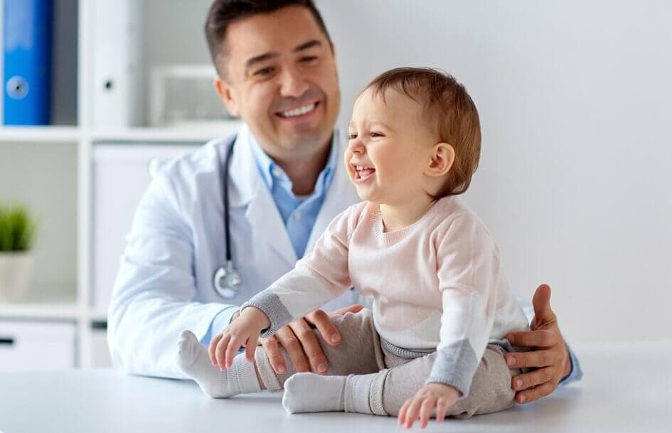 Hispanic doctor holding smiling baby on exam table