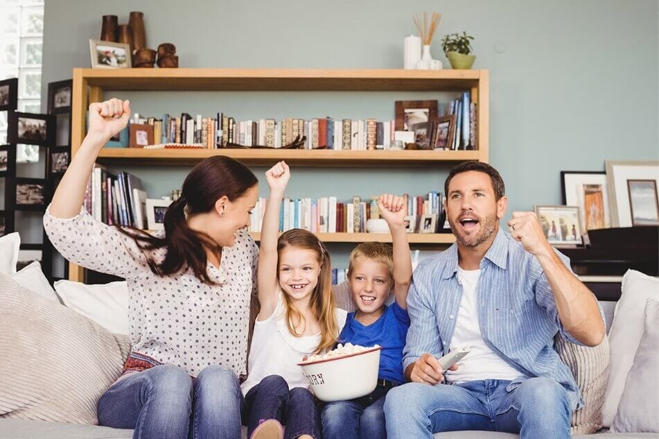 Young family sitting on couch in apartment watching TV and cheering