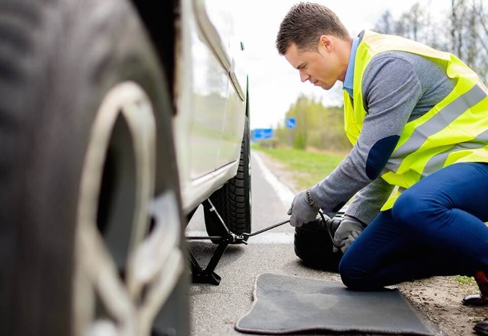 Roadside assistance technician changing flat tire on the side of the road