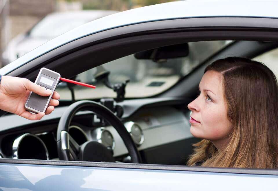 Woman sitting in car being administered breathalyzer test by police officer